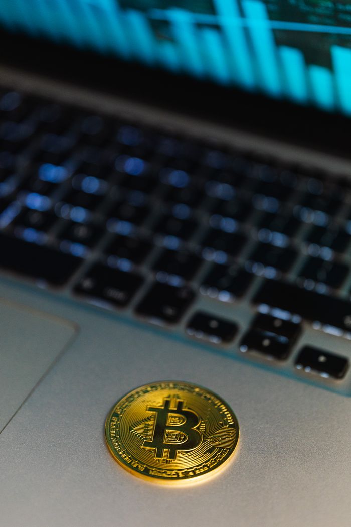 who-we-are Close-up of a Bitcoin coin on a laptop, with a graph display in the background representing cryptocurrency technology.